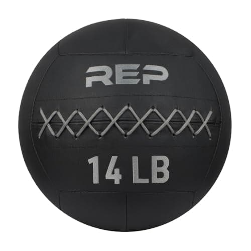 A man carrying a weighted ball past a rack of medicine balls in a gym