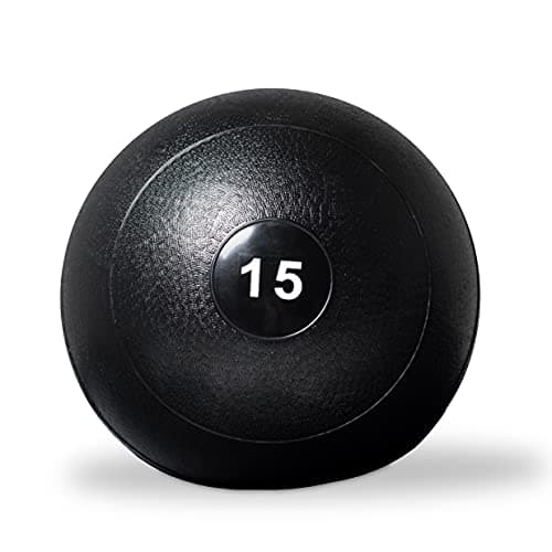 A man carrying a weighted ball past a rack of medicine balls in a gym