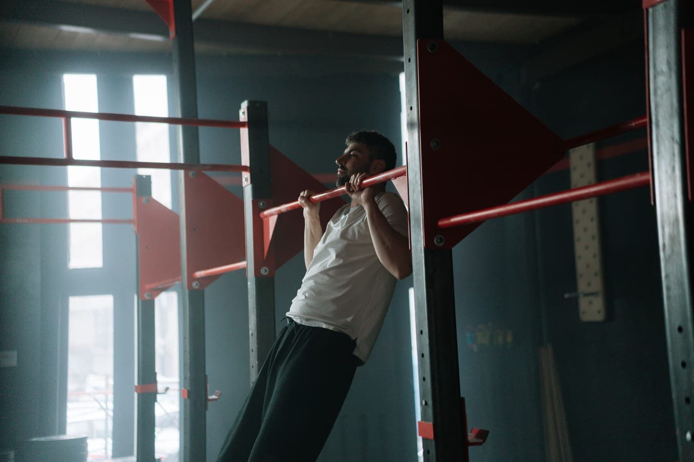 A man doing pull-ups on a bar in a dimly lit indoor training space