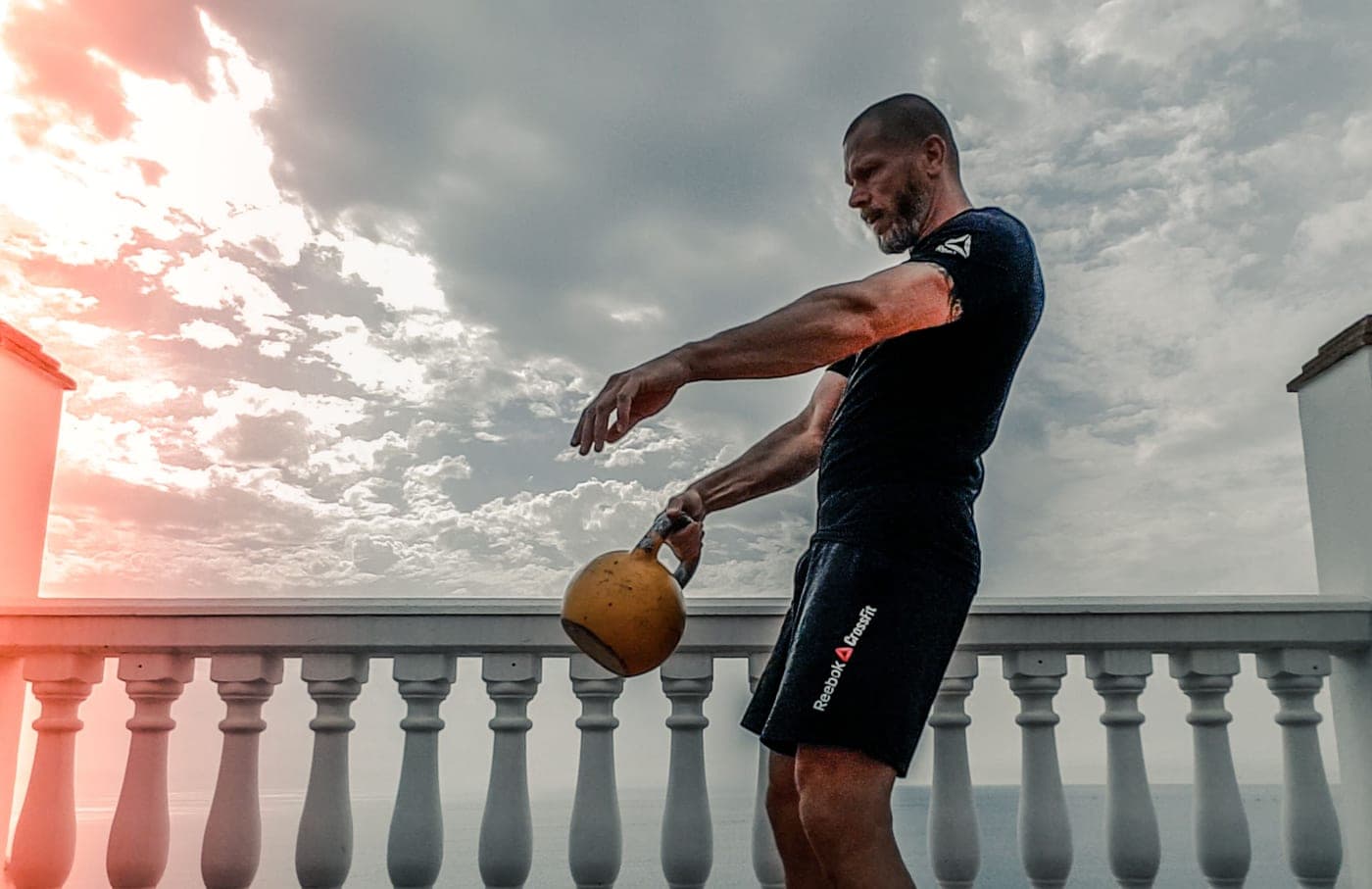 A man doing a kettlebell workout outdoors on a terrace