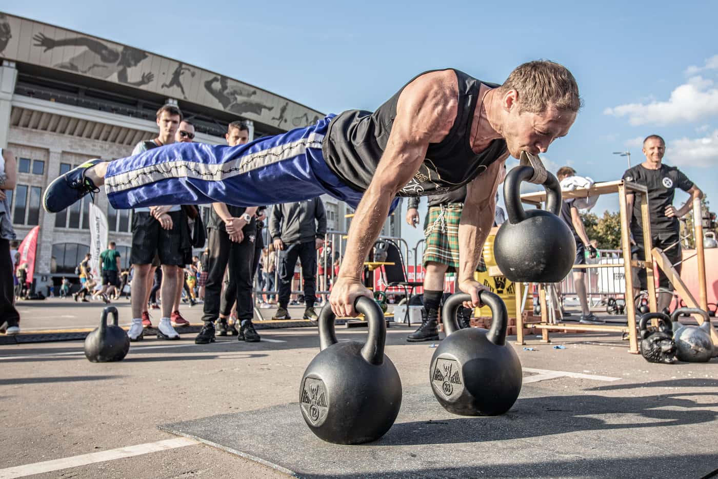 A man balancing on kettlebells at an outdoor fitness event