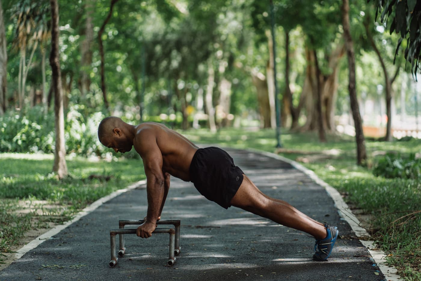A man doing push-ups on low parallel bars in a park