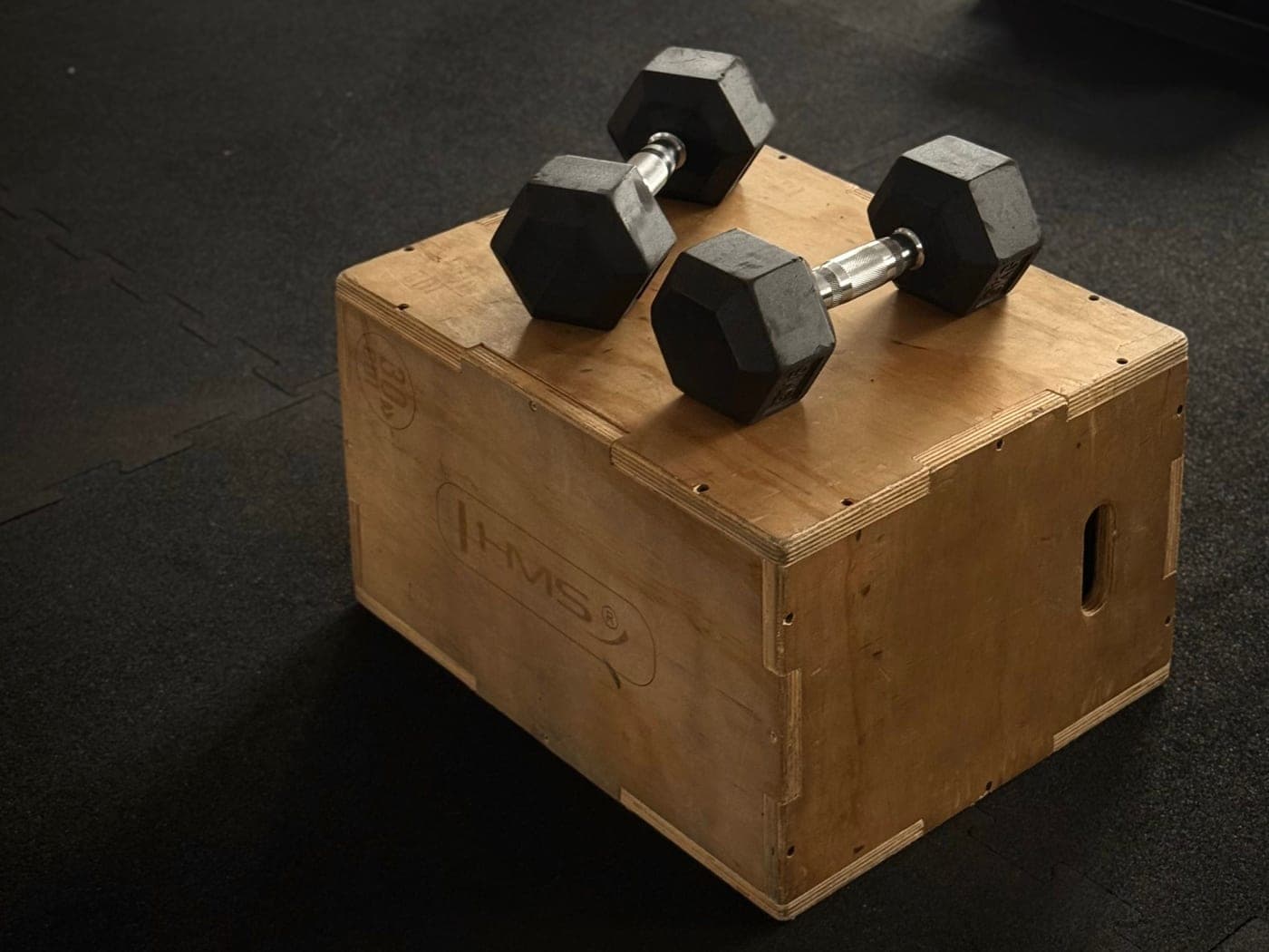 Hex dumbbells resting on a wooden plyo box in a gym