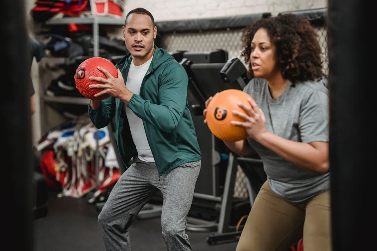 A coach supervising a squat performed with a weighted ball in a gym