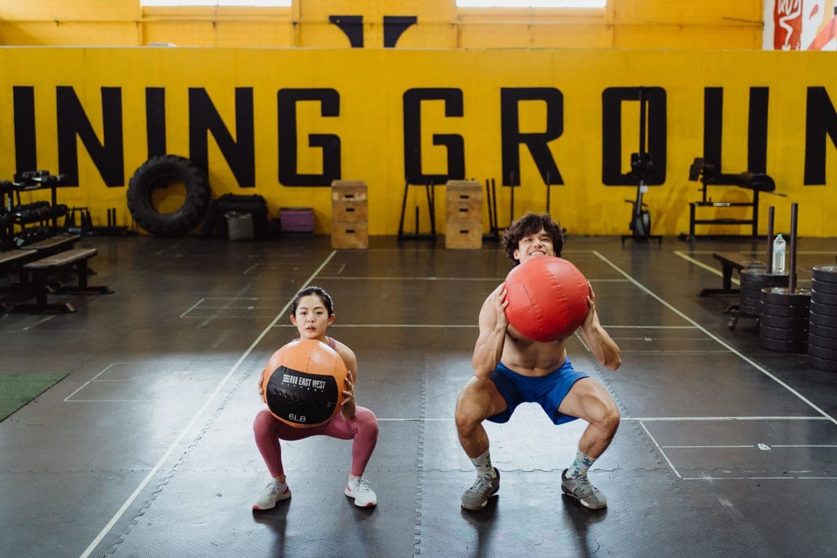 Two people squatting with weighted balls during an indoor workout
